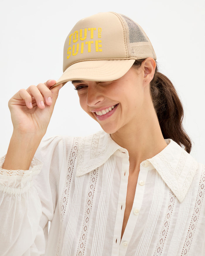 Woman wearing the cream Amélie Blouse and 'Tout de Suite' Trucker Hat.